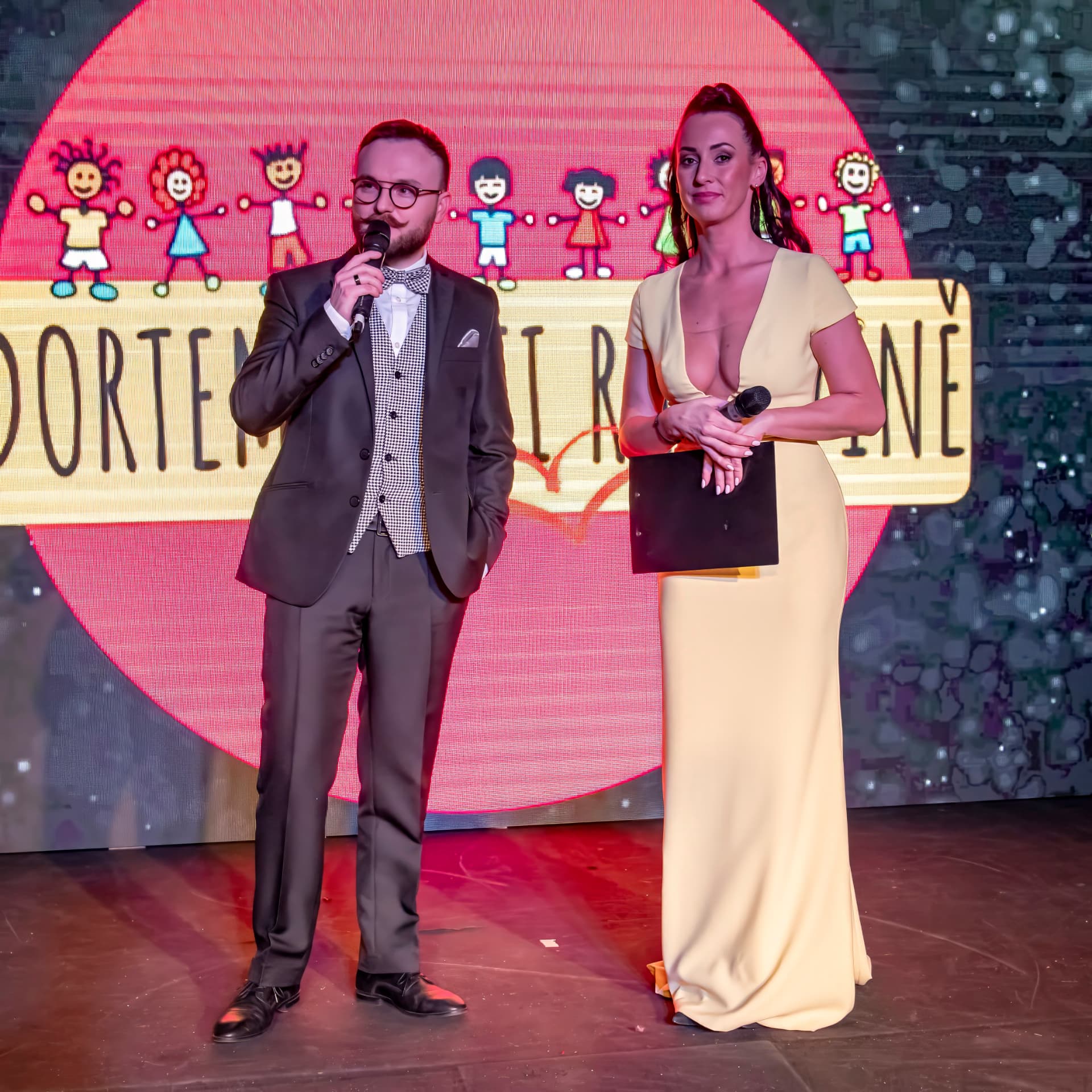 Moderátorská dvojice před obrazovkou s vizuálem 3. charitativního plesu